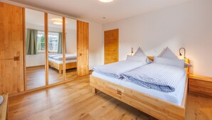 Ein Schlafzimmer mit einem hölzernen Bett, einem Kleiderschrank, einem Spiegel und einem Nachttisch mit einer Lampe.