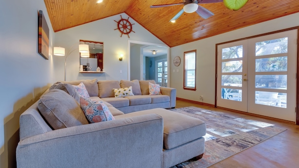 A spacious living room with a large gray sectional sofa, a wooden ceiling, and a view through glass doors. - Serene Pensacola Vacation Rental w/ Gas Grill (Pensacola)