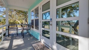 A covered porch with a table and chairs, a door with a doormat, and a view of trees and a parking lot. - Serene Pensacola Vacation Rental w/ Gas Grill (Pensacola)