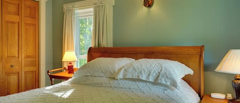Un dormitorio con una cama de madera, una mesita de noche, una lámpara de pared y una ventana con cortinas.