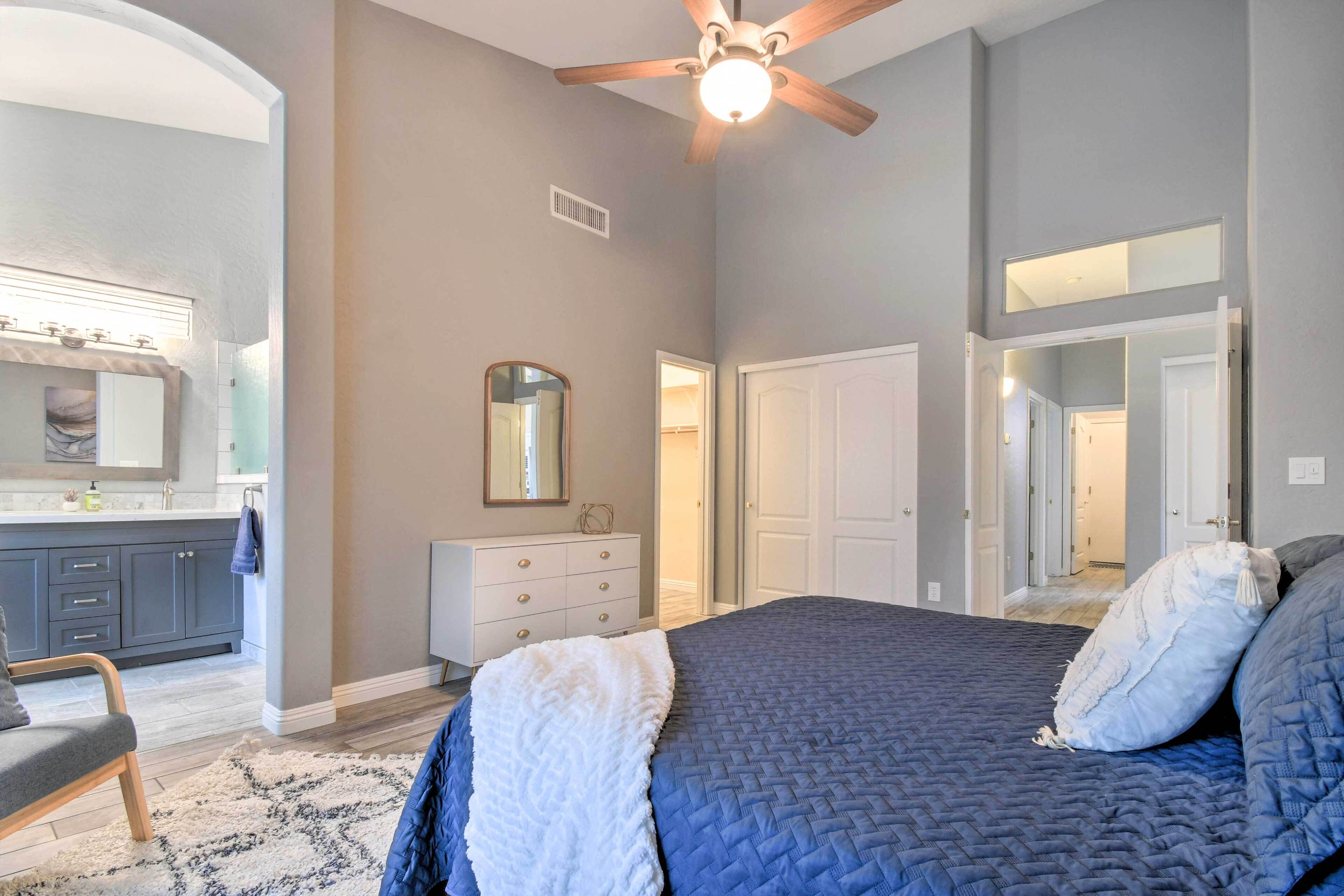 A bedroom with a large bed, a ceiling fan, a dresser, a mirror, and a bathroom visible through an open door.