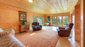 Ein Holzblockhaus-Interieur mit großem Teppich, zwei Ledersesseln, einer Couch und einem Holzkabinett mit Pflanzen.