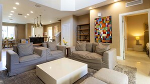 A spacious living room with a neutral color scheme, a white coffee table, and a large abstract painting on the wall. - 1 Mile to Disney: Modern Townhouse in Magic 3114 (Kissimmee)