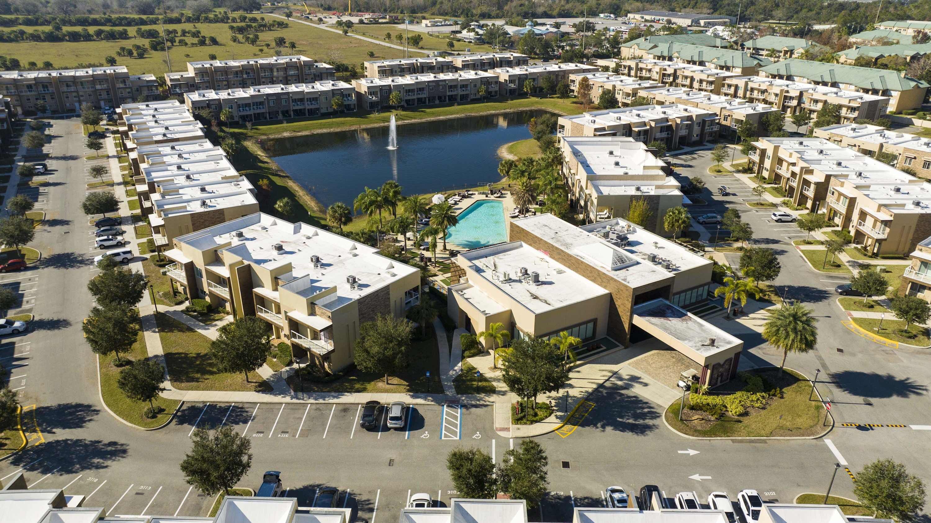 An aerial view of a residential complex with multiple apartment buildings, a central swimming pool, and a parking area.
