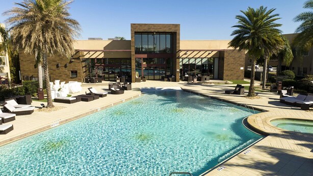 A pool area with lounge chairs and palm trees, surrounded by a building with large windows and a modern design. - 1 Mile to Disney: Modern Townhouse in Magic 3114 (Kissimmee)