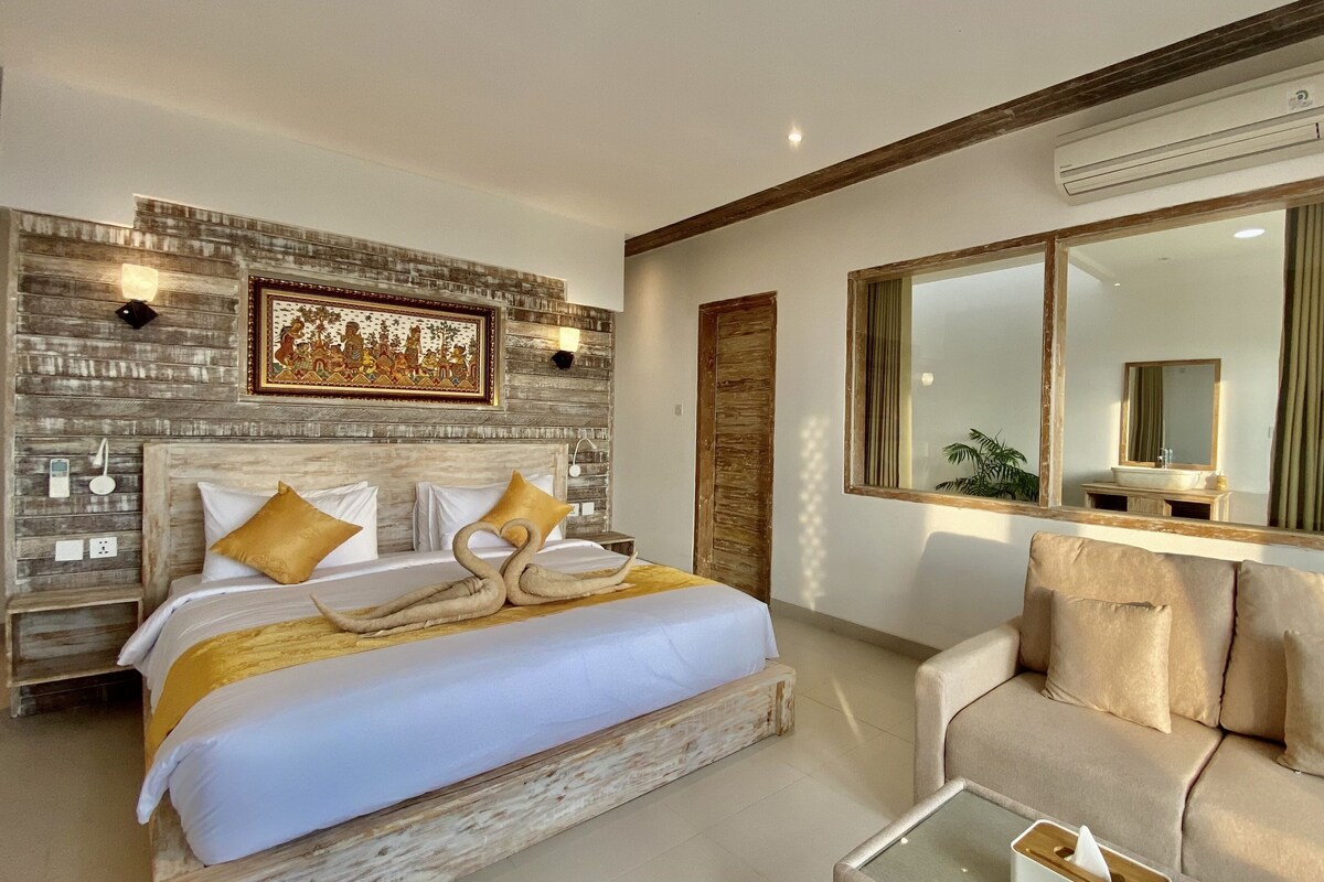 A hotel room with a bed, a sofa, a large mirror, and a wall-mounted air conditioner.