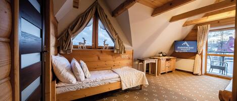 Un dormitorio con cama de madera, un escritorio, televisión y vista a ciervos fuera de la ventana.