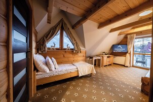 Un dormitorio con cama de madera, un escritorio, televisión y vista a ciervos fuera de la ventana.