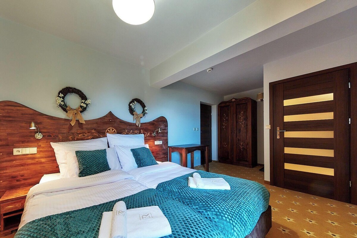 A bedroom with a wooden headboard, two wall-mounted wreaths, a bed with white and teal bedding, a nightstand, and a wardrobe.