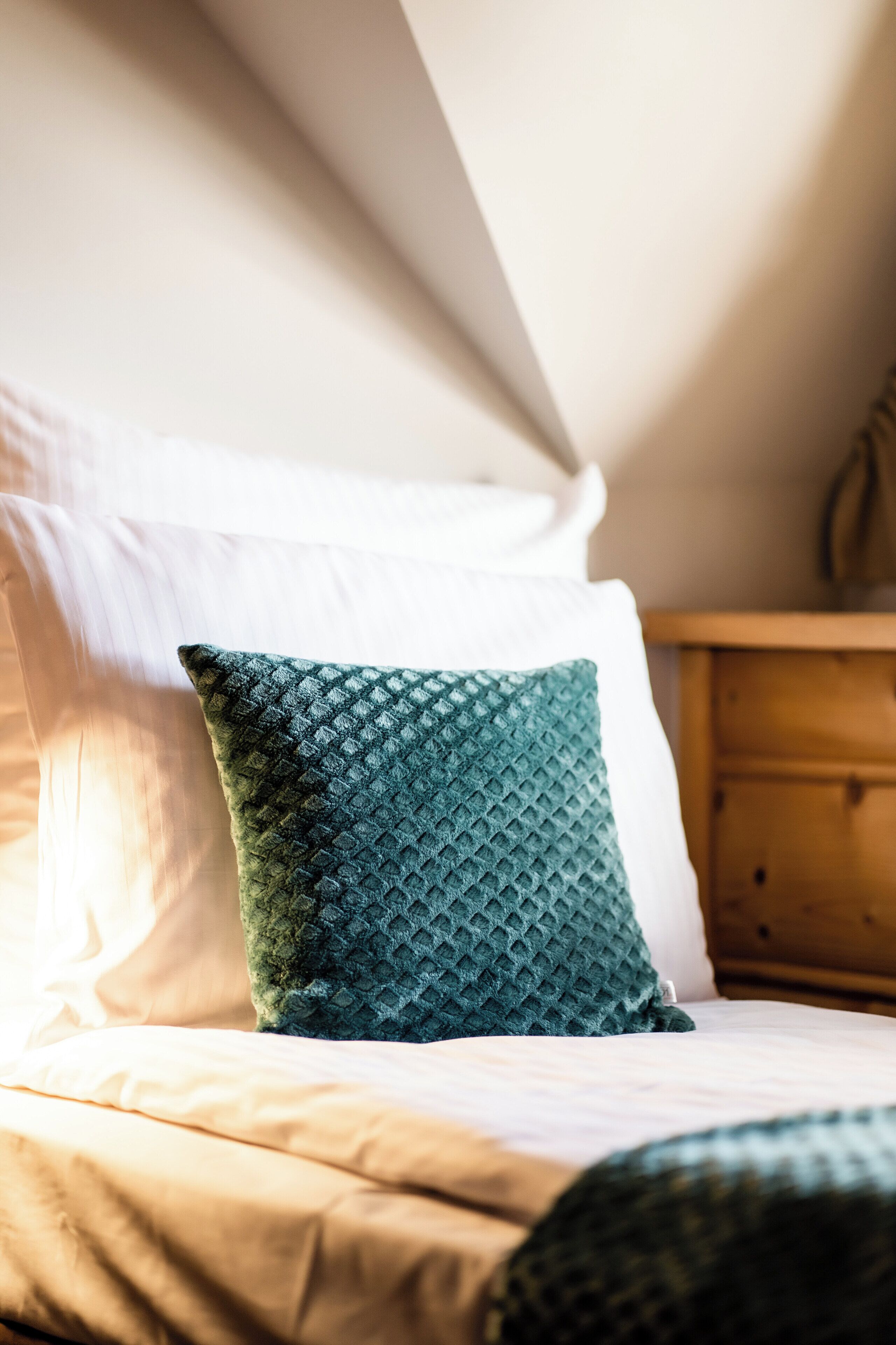 Una cama con un cojín verde con textura, ropa de cama blanca y una mesita de noche de madera.