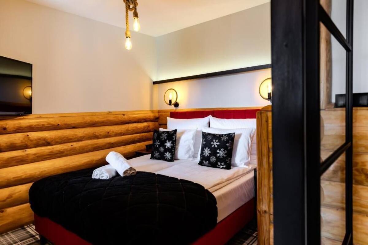 Ein Hotelzimmer mit einem hölzernen Kopfteil, einem Bett mit weißer Bettwäsche und schwarzen Kissen in Schneeflockenform, einer schwarzen Tagesdecke und einem flachbildfernseher an der Wand.
