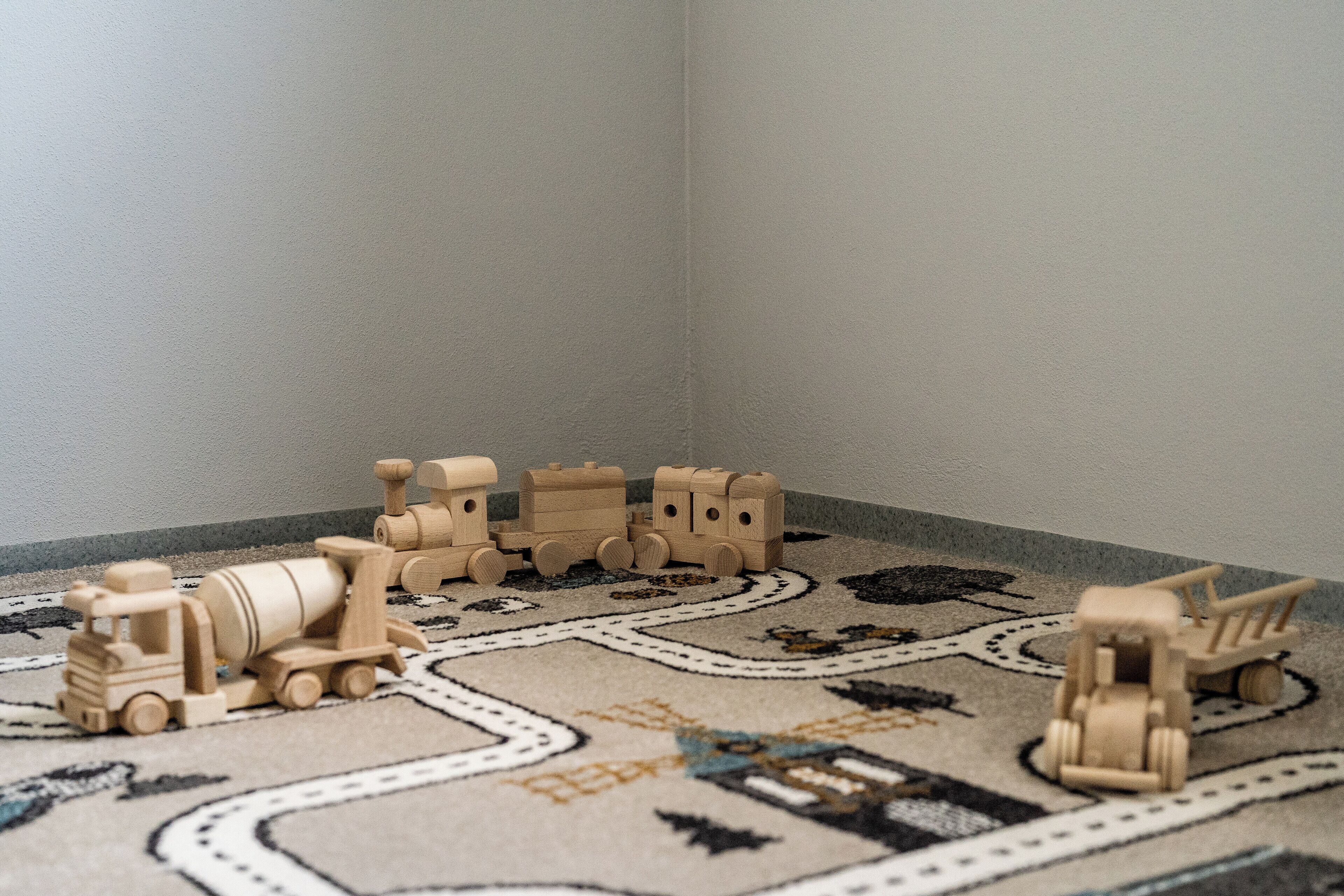 Esquina de una habitación con una alfombra estampada y trenes de juguete de madera.