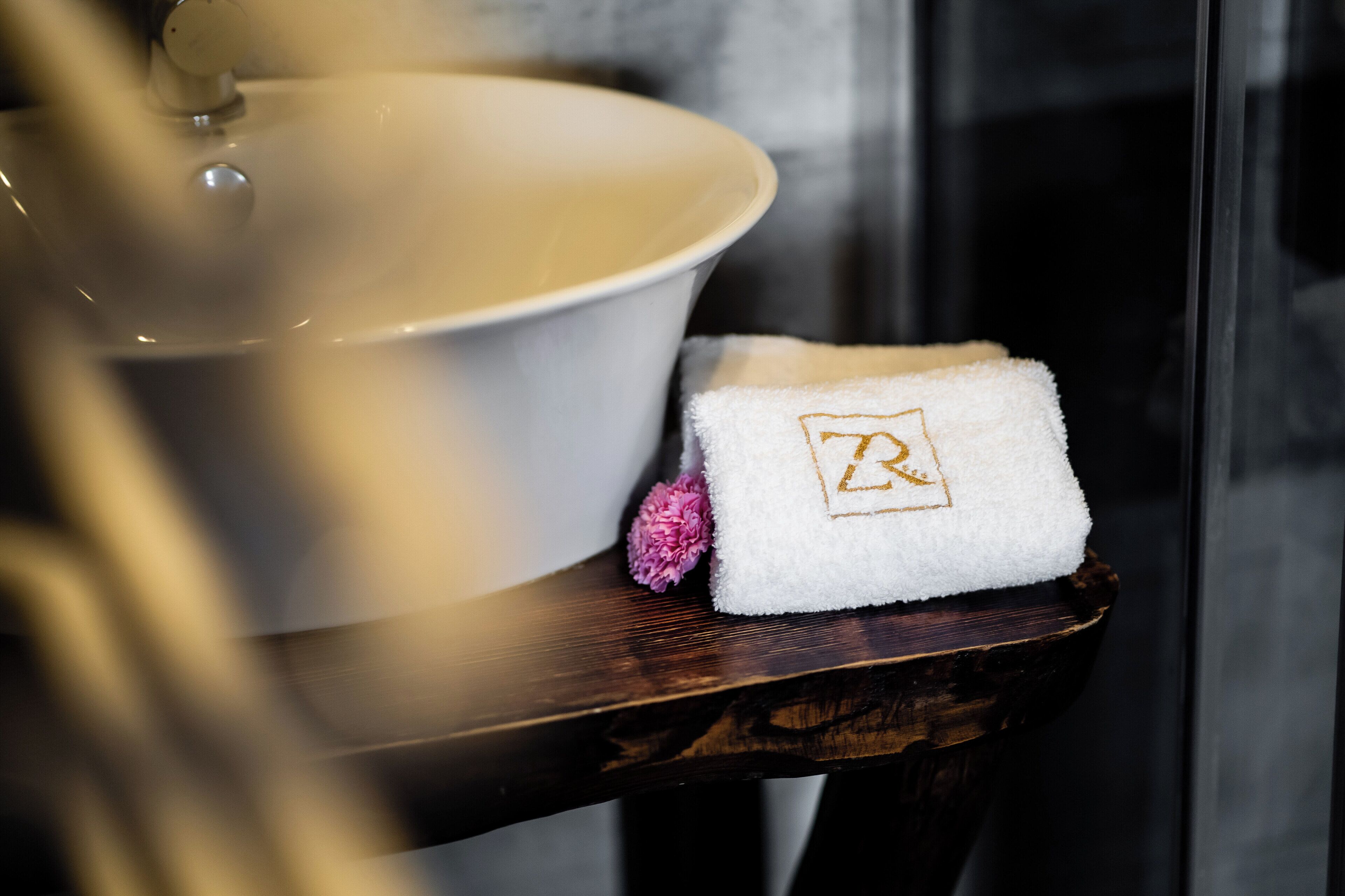 A white bathtub with a lid, a white towel with a gold monogram, and a pink flower on a wooden tray.