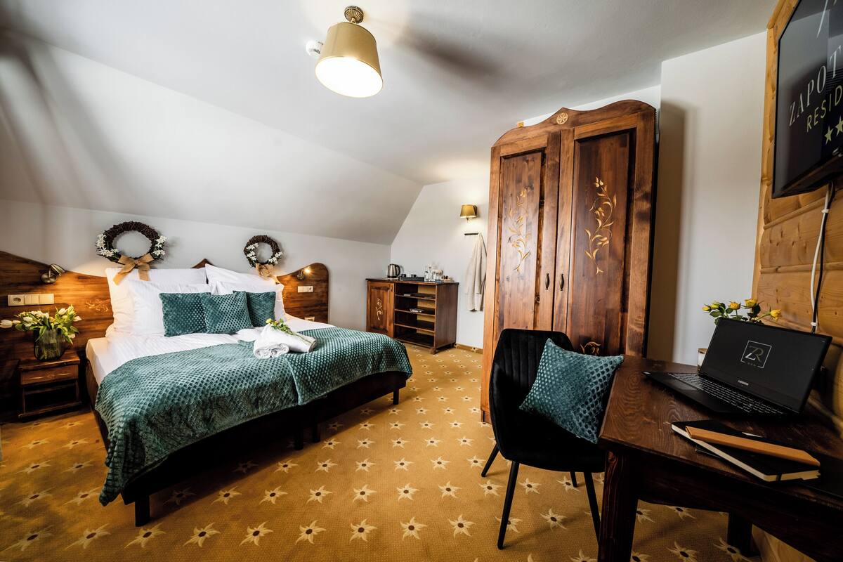 Ein Schlafzimmer mit einem Bett, einem Schreibtisch mit Laptop, einem Kleiderschrank und einem an der Wand befestigten Fernseher.
