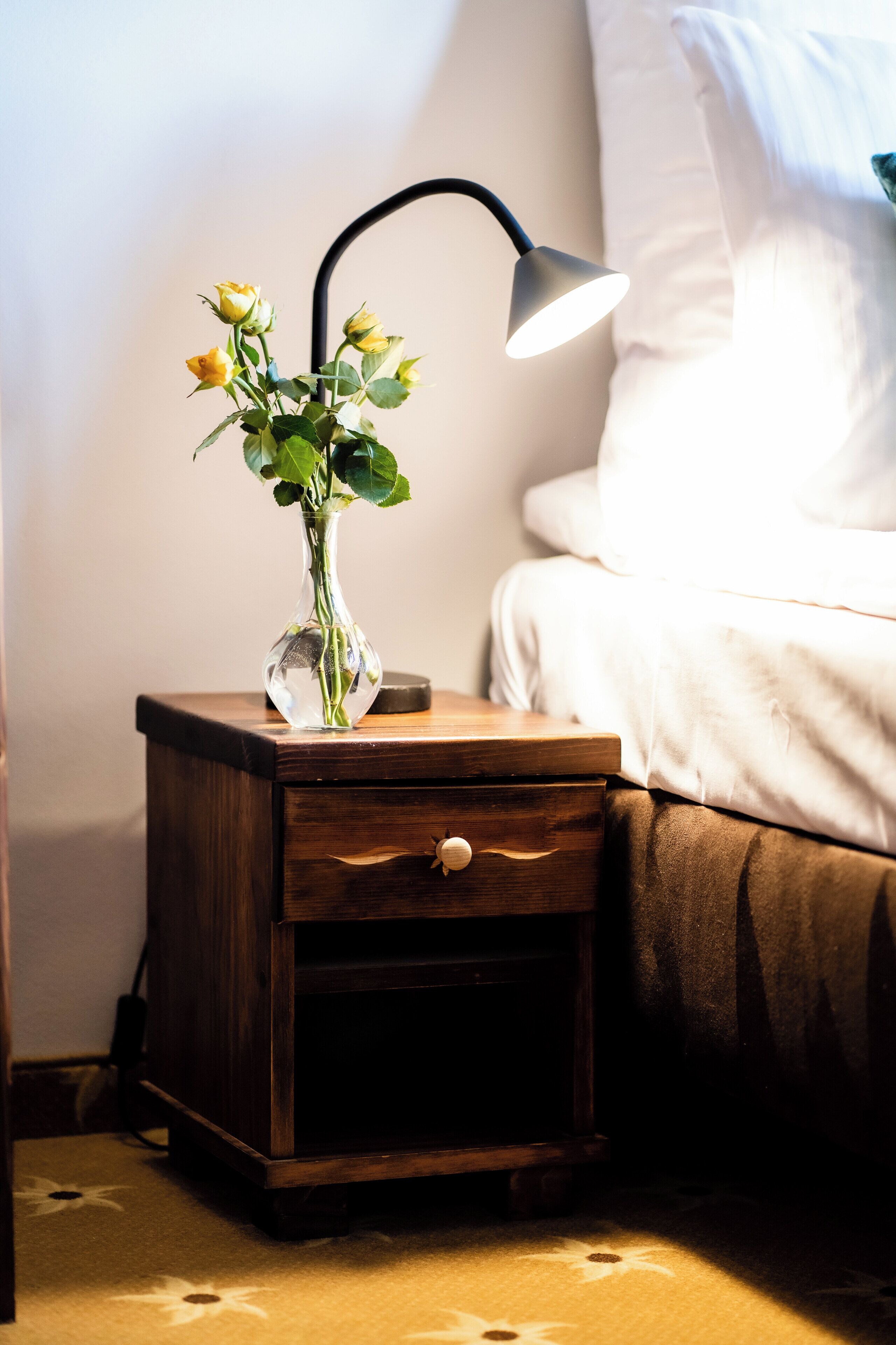 A bedside table with a vase of flowers and a lamp.