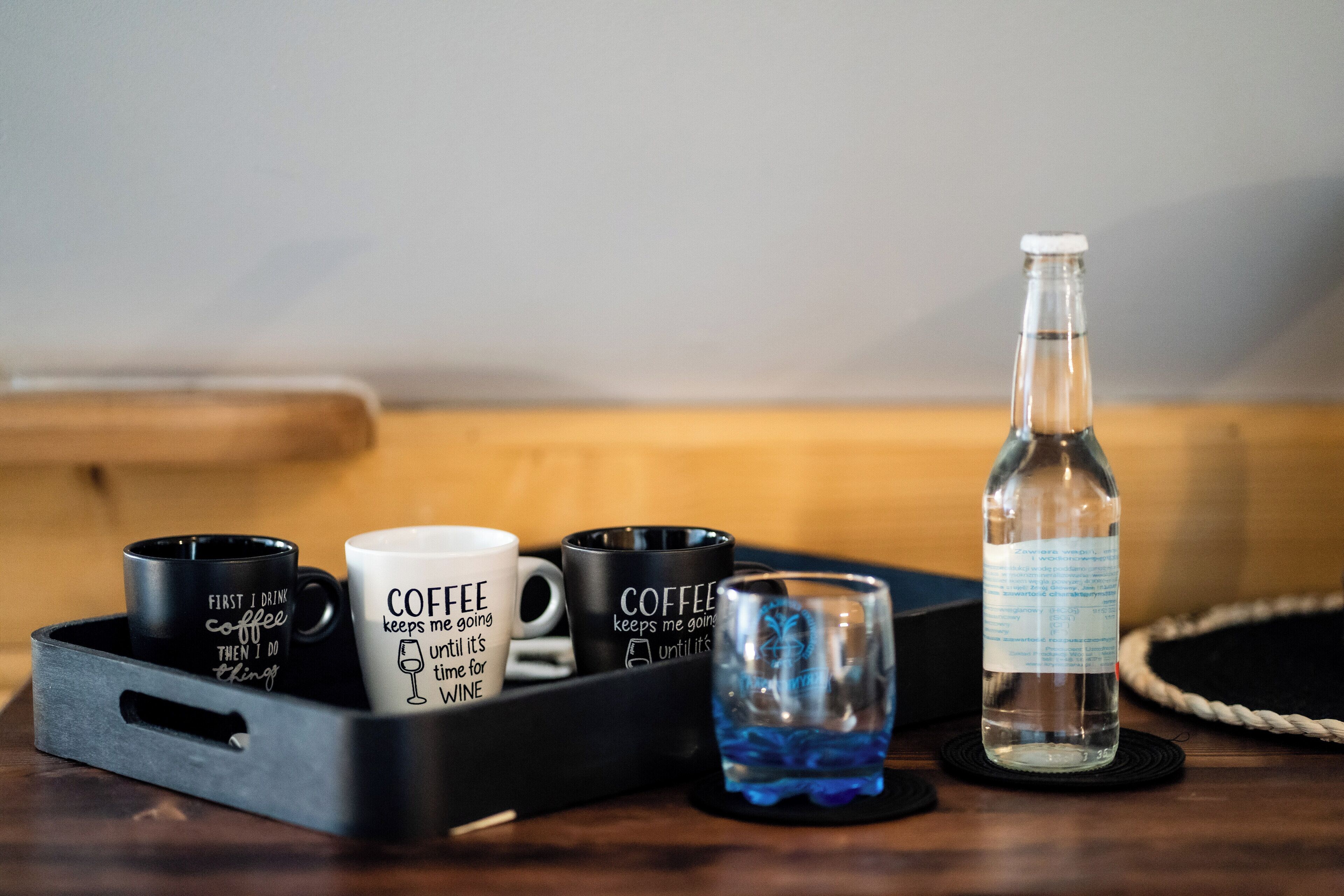 A tray with three coffee mugs and a glass on a wooden table.