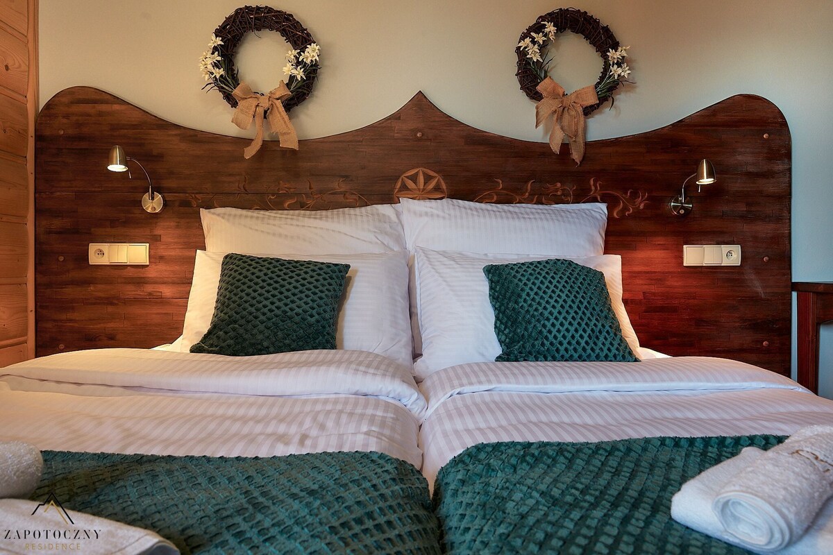 A double bed with a wooden headboard, two wall sconces, and two decorative wreaths.