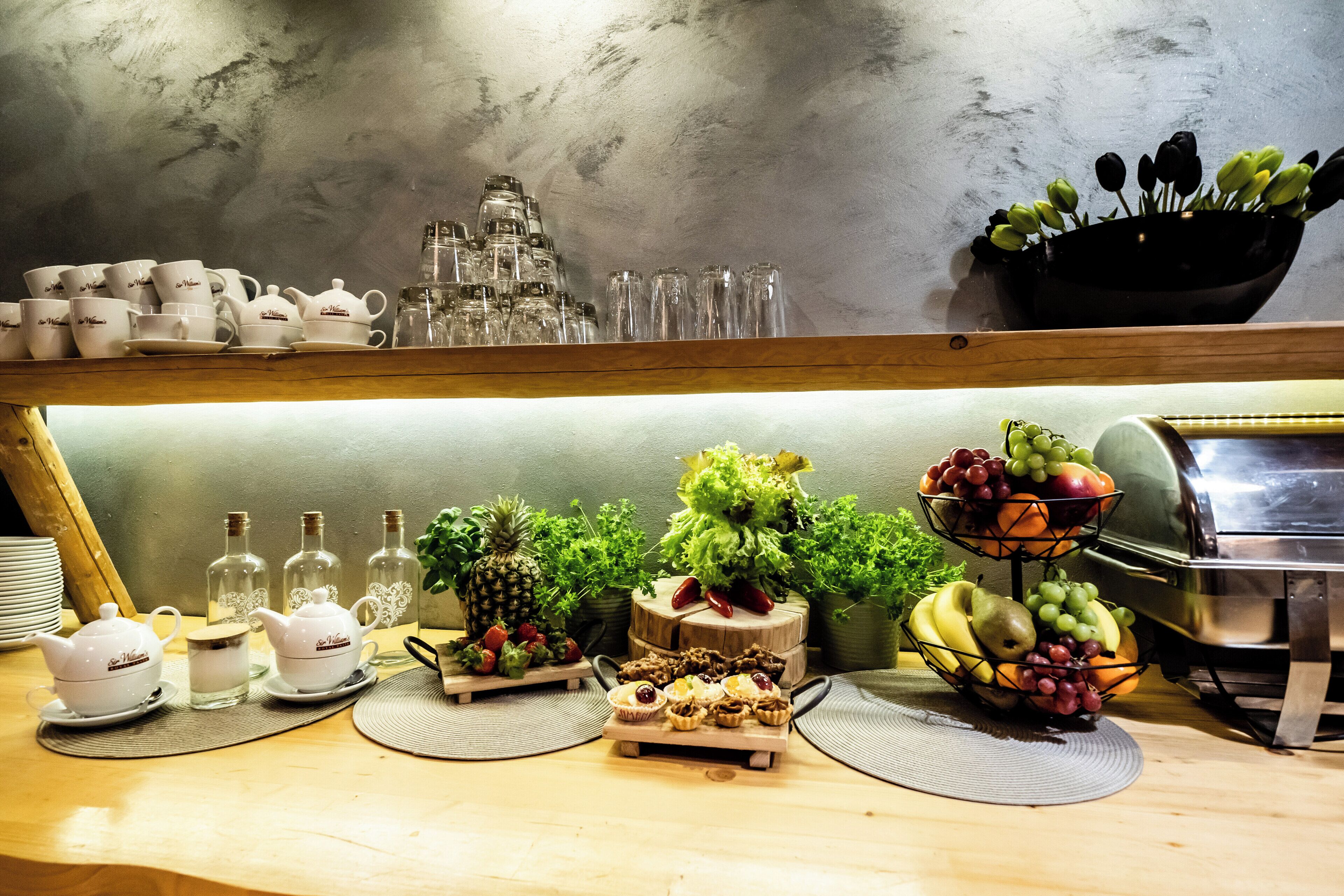Un bufé de desayuno con diversas opciones de comida, entre ellas frutas y pastelería, así como una selección de teteras y tazas de té blancas.