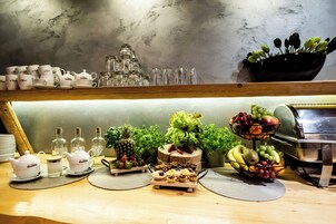 Un bufé de desayuno con diversas opciones de comida, entre ellas frutas y pastelería, así como una selección de teteras y tazas de té blancas.