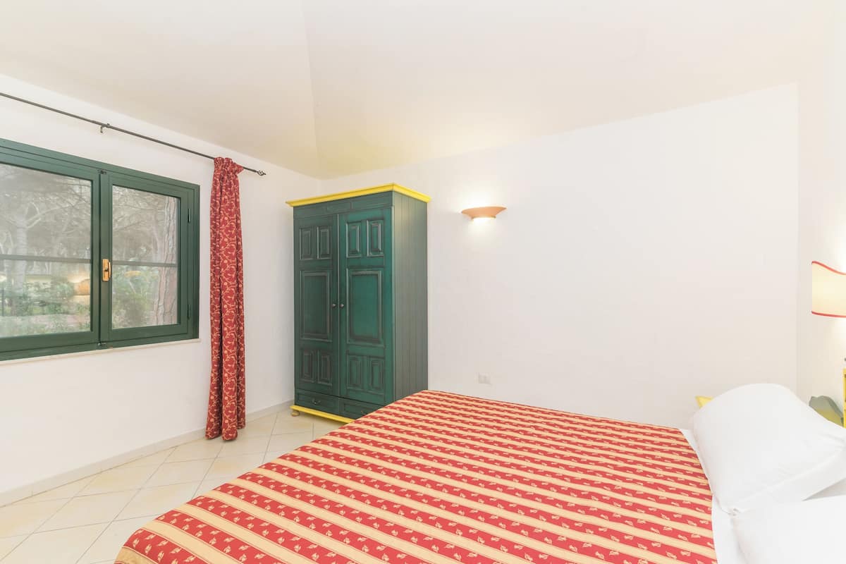 Een slaapkamer met een bed, een kledingkast, een raam met gordijnen en een wandlamp.