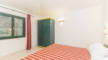 Un dormitorio con cama, armario, ventana con cortinas y una lámpara fijada a la pared.