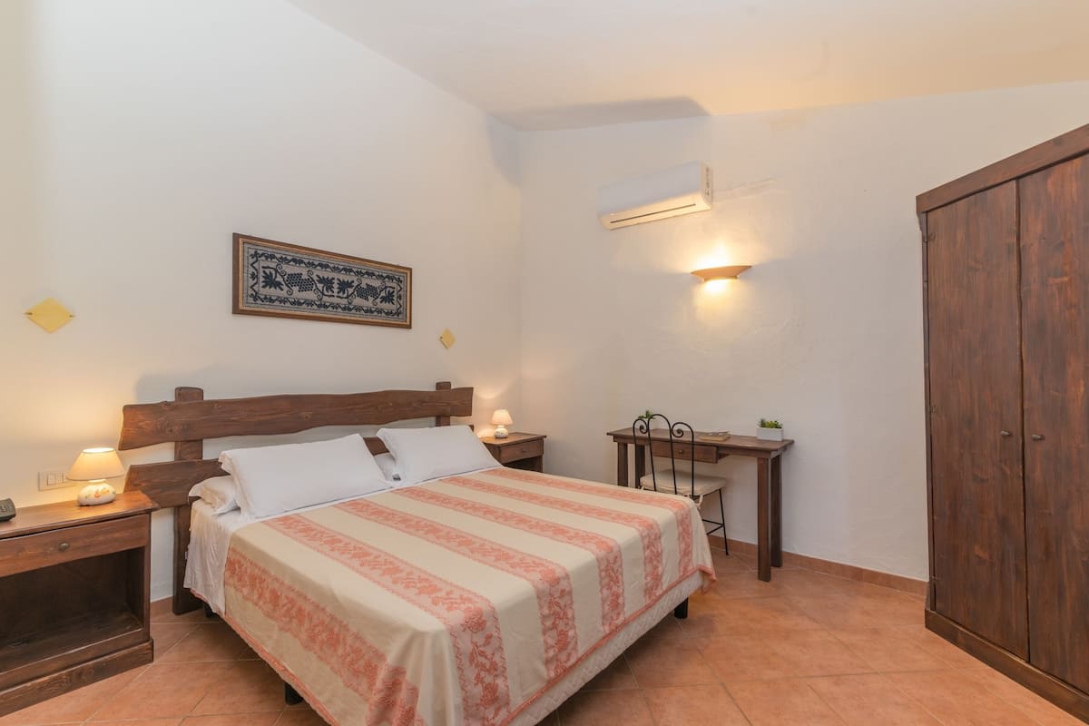Een slaapkamer met een bed, nachtkastjes, een bureau, een airconditioning en een kledingkast.