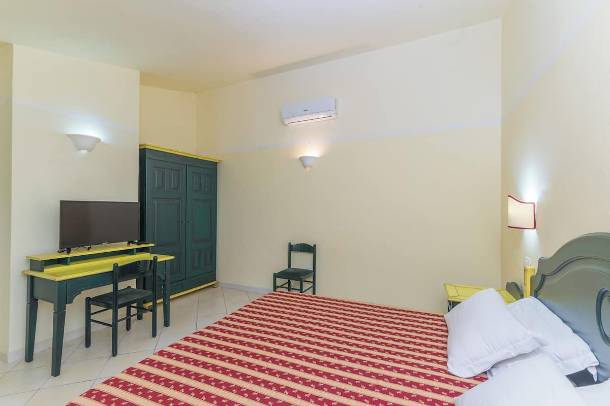 Een slaapkamer met een bed, een bureau, een stoel, een kledingkast en twee wandlampen.