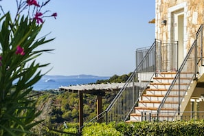 Un bâtiment en pierre avec un escalier menant à une terrasse en bois d’où l’on peut admirer un paysage côtier.