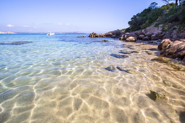 Une plage dégagée, avec des rochers, un bateau et une côte visible au loin.