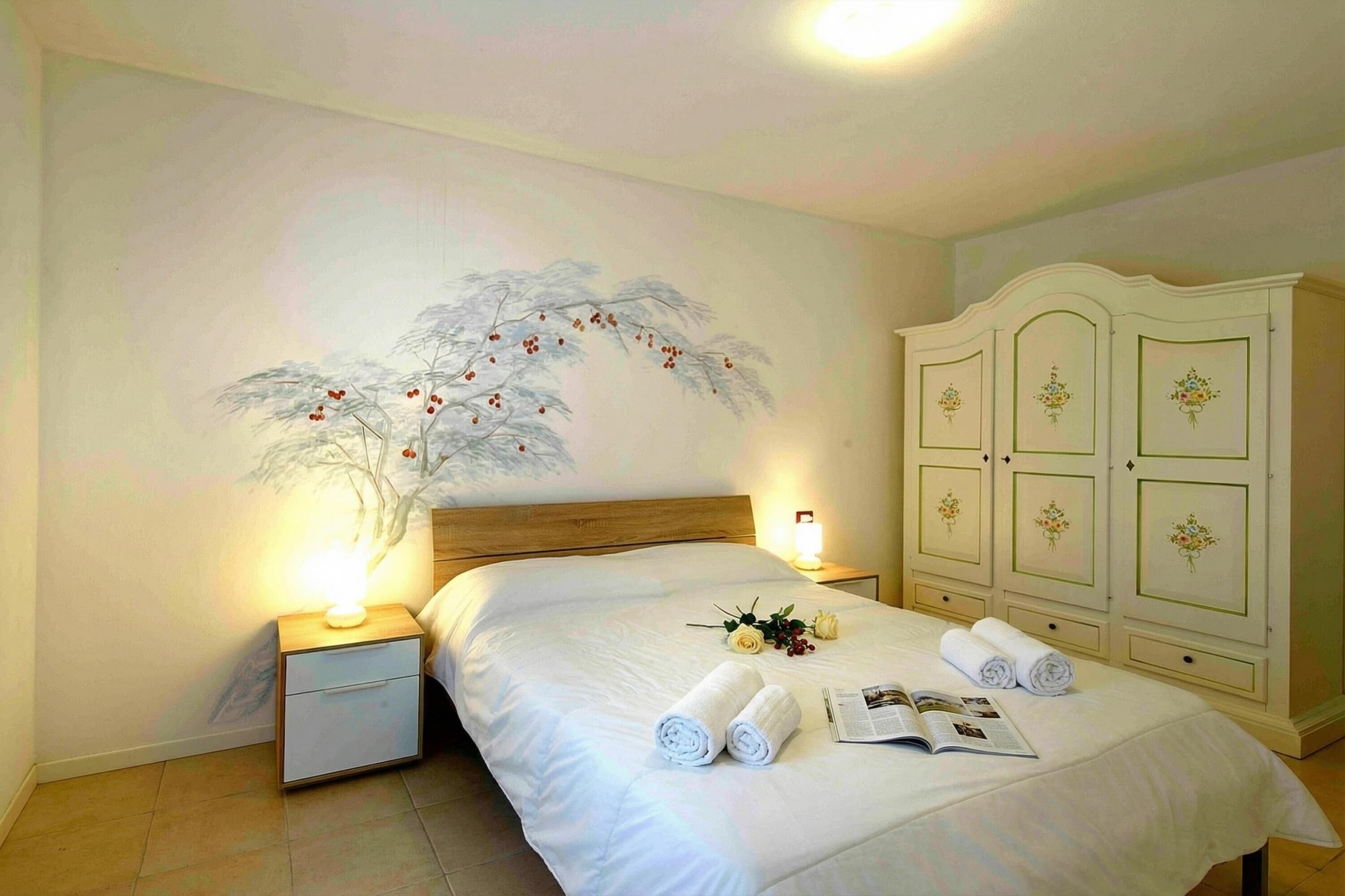 A bedroom with a bed, nightstands, a wardrobe, and a wall painting.