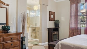 Quarto com uma cama grande, penteoudeir, mesa de vaidade, espelho, lareira e área de chuveiro.