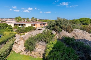 A large house with a tiled roof, surrounded by greenery and rocks.