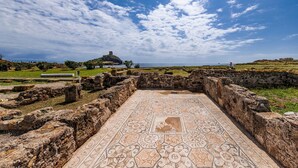 Ruinas antiguas con piso estampado y paredes de piedra, mostrando una colina distante con restos.