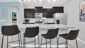 Une cuisine moderne avec des meubles de couleur sombre, un réfrigérateur en acier inoxydable et un plan de travail en marbre.