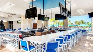 Un espace bar moderne avec un long comptoir, des tabourets de bar bleus et blancs, et plusieurs téléviseurs à écran plat fixés au plafond.