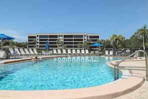 A swimming pool with lounge chairs and umbrellas, a building in the background, and a clear sky. - Intracoastal Views, Boat Dock, Beach Access, Pool (Sarasota)