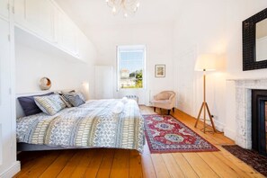 A bedroom with a large bed, a standing lamp, a chair, and a fireplace.