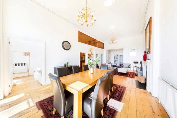 A spacious dining area with a wooden table and chairs, a chandelier, and a view into the kitchen.