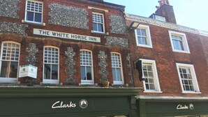 Een gebouw met een bord waarop 'The White Horse Inn' staat en een winkel van 'Clarks' met een uitverkoopbord.
