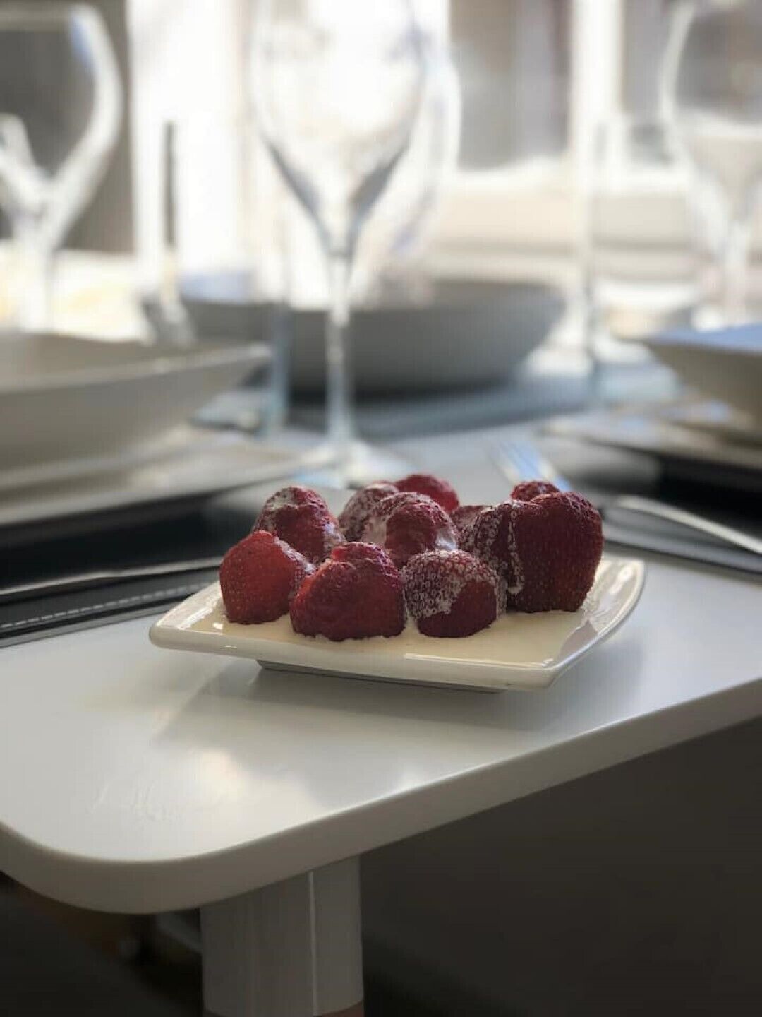 Une assiette blanche avec des framboises posée sur une table.