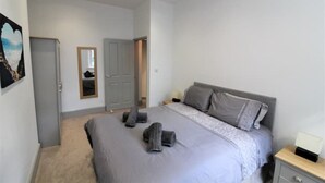 Een slaapkamer met een bed, nachtkastje, kledingkast, deur en een schilderij aan de muur.