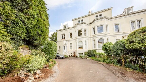 A large, two-story building with a symmetrical facade, a driveway leading to the entrance, and a well-maintained garden with various shrubs and trees. - Clifton Spacious 3 Bed Apt&Parking-Simply Check In (Bristol)