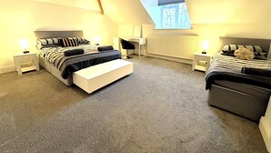 A modern bedroom with a loft-style ceiling, a large bed with a bench, a desk, and a chair. - Clifton Spacious 3 Bed Apt&Parking-Simply Check In (Bristol)