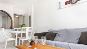 A living room with a grey sofa, a wooden table with three wine glasses, and a white dining table with chairs. - Jardines Family 204 by Interhome (Salou)