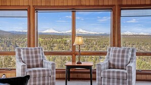 A cozy room with two plaid armchairs facing a large window overlooking a snowy mountain and forest.