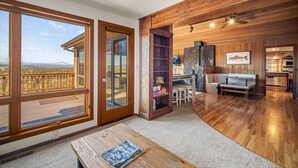 A spacious living area with a large wooden table, a stone fireplace, and a kitchen visible through an open door.