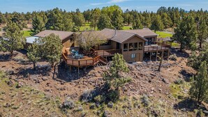 A large wooden cabin with a deck, surrounded by trees and rocky terrain.
