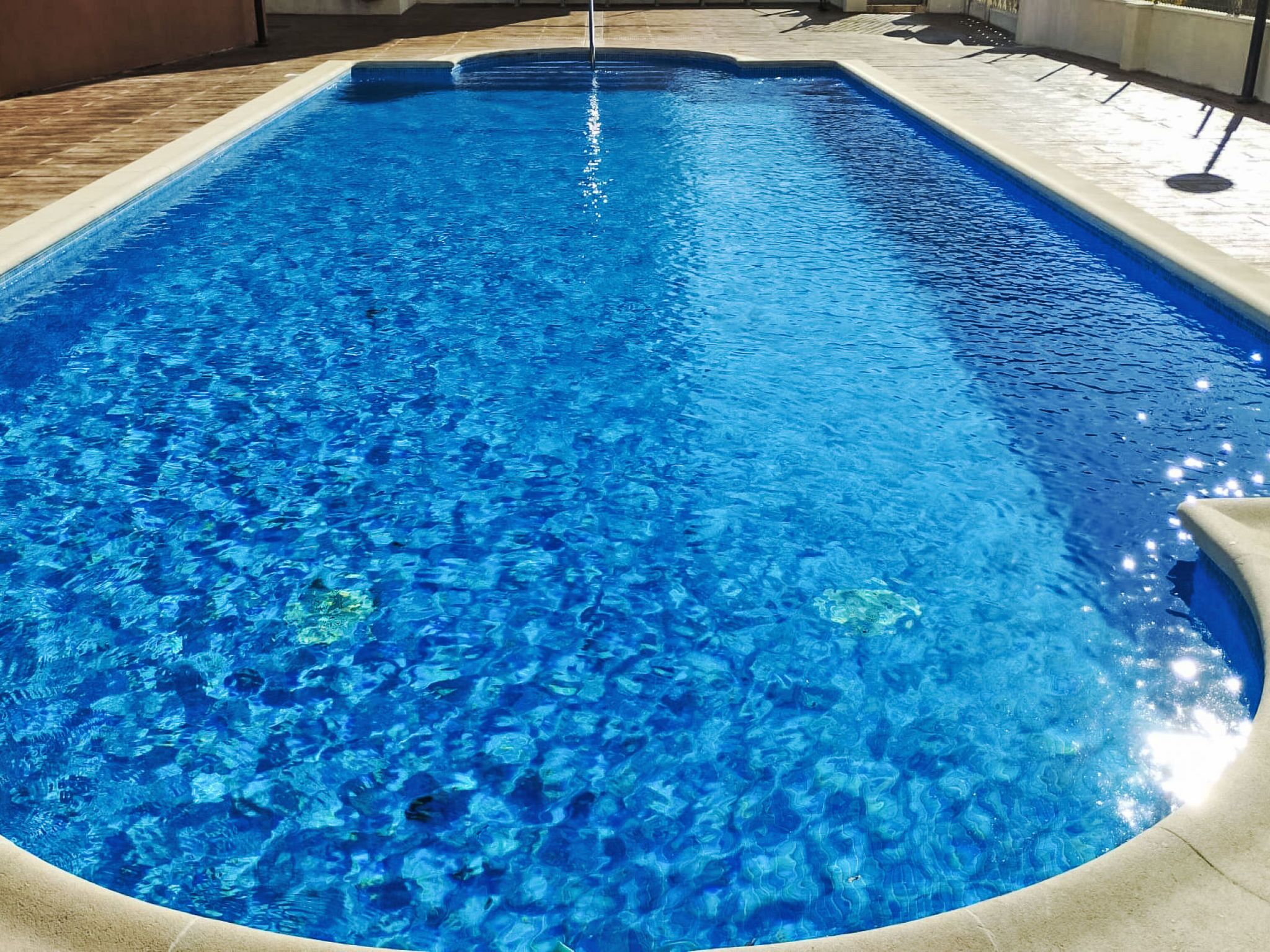 A rectangular swimming pool with clear blue water, surrounded by a tiled deck.