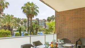 Un balcón con mesa lista para comer, sillas y vistas a palmeras y edificios.