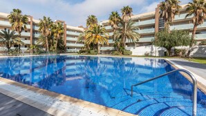 Una piscina con agua cristalina azul, rodeada de palmeras y un edificio de varios pisos con balcones.